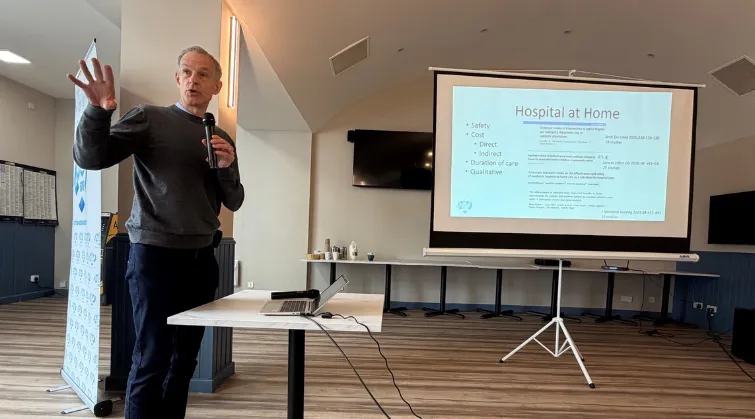 President Steve Turner speaks in front of a projector about hospital at home services
