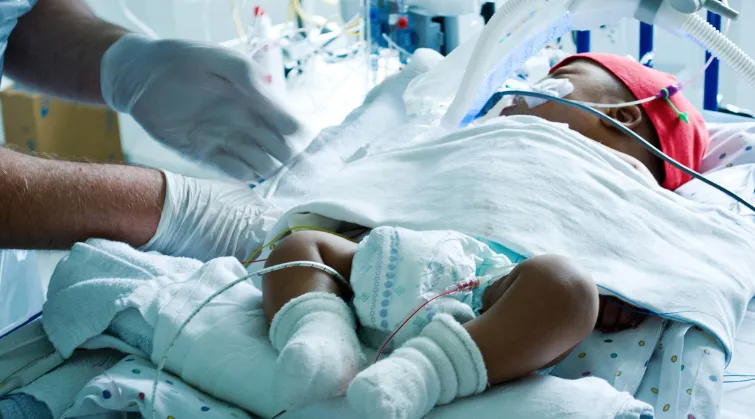 critically sick baby in incubator with tubes