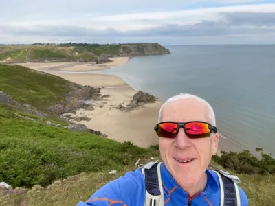 Dr David Evans walking by a sandy beach with a clear sky and blue waves