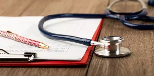 Stethoscope with clipboard, paper and pen on a wooden surface