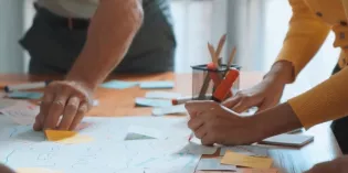 Close up of people around a table, using post-its on paper in a collaborative way