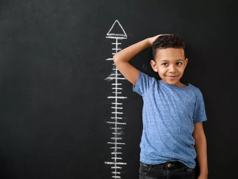 Young boy measures his height against blackboard