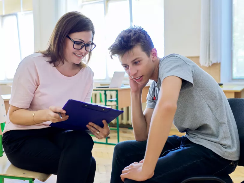 Woman health professional with a clipboard speaking with a teenage boy, in a school or community centre
